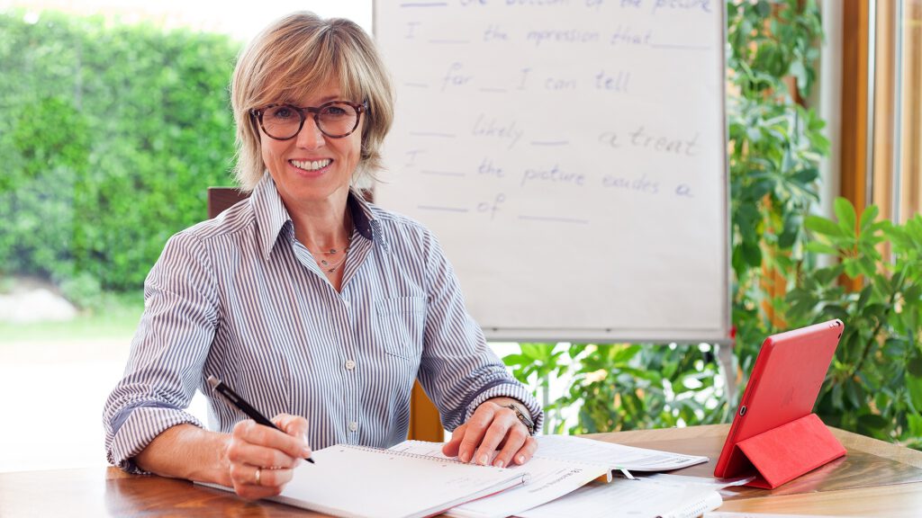 Monika Lukas sitzt am Schreibtisch mit einem Ipad und ein Flipchart im Hintergrund